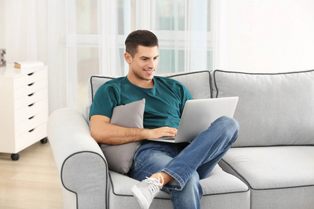 英俊的人使用膝上型电脑在沙发上休息在家照片