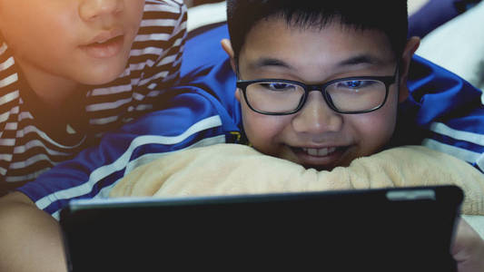 愉快的亚洲小孩子看着平板电脑与微笑的脸