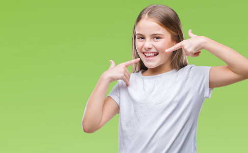 年轻美丽的女孩在孤立的背景下微笑着自信地显示和指着手指的牙齿和