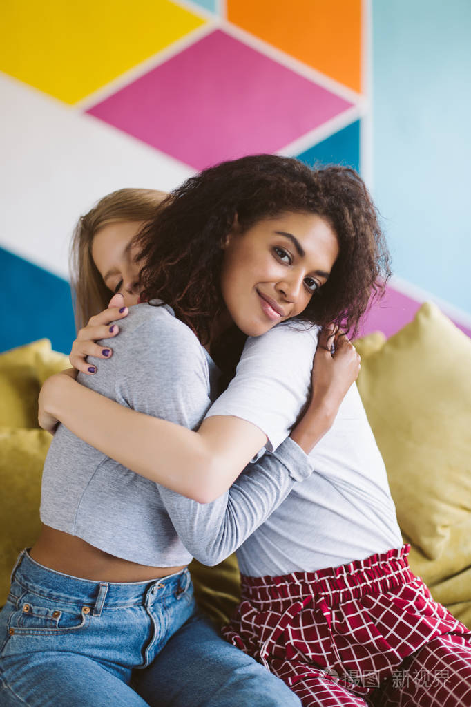 年轻的微笑非洲裔美国人妇女与深色卷曲的头发拥抱女朋友朦胧地看在