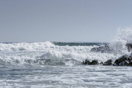 海浪在海滩岩石上撞击着简单的地平线和清澈的天空。海滩溅浪