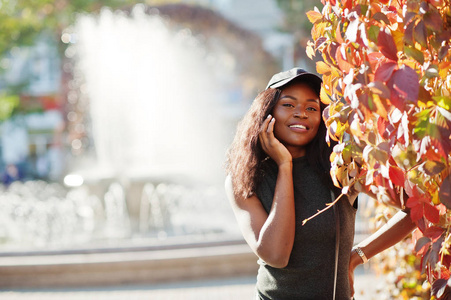时尚的非洲裔美国女孩在帽子摆在阳光明媚的秋日反对红叶。非洲模范妇女