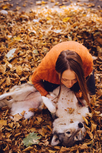 年轻的红头发女孩正在玩她的秋天落叶堆成一堆的大狗