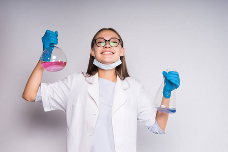 家用化学愉快的年轻女孩化学家用玻璃和长袍拿着烧瓶与化学制品在手