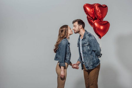 年轻夫妇的侧面视图能够亲吻, 而男子抱着红色的心形气球孤立在灰色