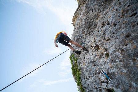 从下面拍摄的男性登山者攀登山墙在惊人的晴天