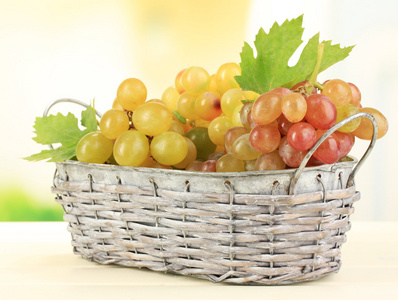 在木桌上,自然背景上的篮子里成熟甜葡萄照片