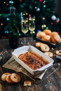 一个喜庆的新年餐桌, 奶酪蛋糕, 巧克力, 橘子, 葡萄, 饼干, 香槟和两个眼镜的背景下装饰圣诞树灯
