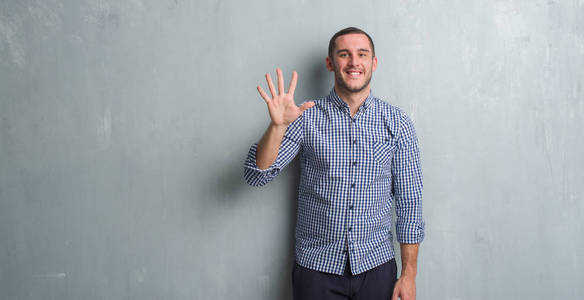 年轻的白种人在灰色的垃圾墙显示和指向五的手指, 而微笑的信心和快乐