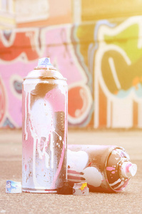一些用粉红色和白色油漆和帽子的喷雾罐在压力下喷涂油漆是躺在沥青附近的彩绘画墙在彩色涂鸦图纸