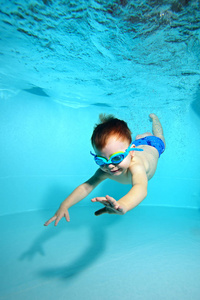 小男孩戴着眼镜游泳潜到水底的水池底。肖像.垂直方向