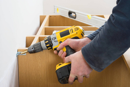 工人手把螺丝拧到白墙上照片