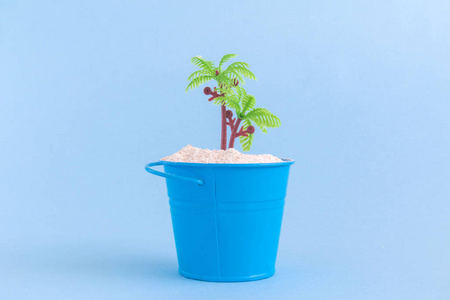 罐头与沙子和塑料棕榈树隔绝在蓝色背景。夏日假期简约静物概念