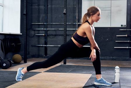 美丽的年轻女子的侧面图伸展腿热身前 crossfit 运动在现代健身房