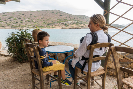 母亲与儿子坐在海边面对户外餐厅