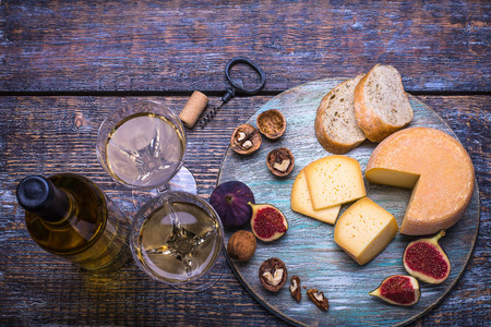 白葡萄酒瓶, 酒杯, 软木, 瓶螺丝和一套产品奶酪, 葡萄, 坚果, 橄榄, 无花果, 面包在木板上, 背景