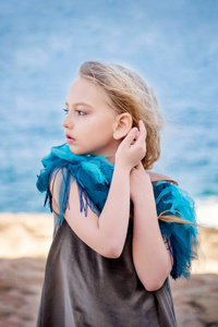 特写肖像一个可爱的小金发女孩凝视着遥远的大海朦胧的姿态与她的手靠近她的耳朵