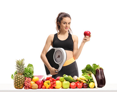 健身妇女体重秤和一个苹果在桌子后面的水果和蔬菜在白色背景下隔离