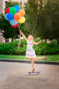 愉快的小女孩滑冰在一个 scateboard 与大堆氦填充五颜六色的气球在公园