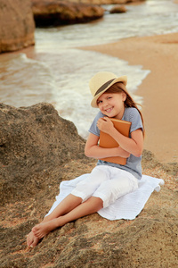 白种人微笑着年轻的女孩穿着休闲服夏季一天读一本书在海滩上