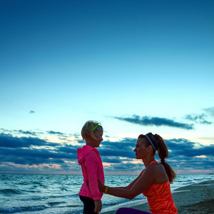 健康的母亲和孩子在体育样式衣裳在海滩在日落