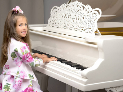 漂亮的小女孩正在玩一架白色的大钢琴