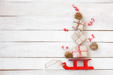 圣诞红雪橇由礼品盒, 金色锥体, 白色木桌上的彩带, 复古风格, 从上面的看法, 新年作文