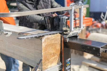 锯木厂用锯机在防护手套上裁剪的木匠形象.木制原木被锯切照片