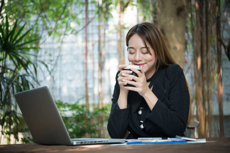 年轻美丽的商业妇女在笔记本电脑上享受咖啡的工作