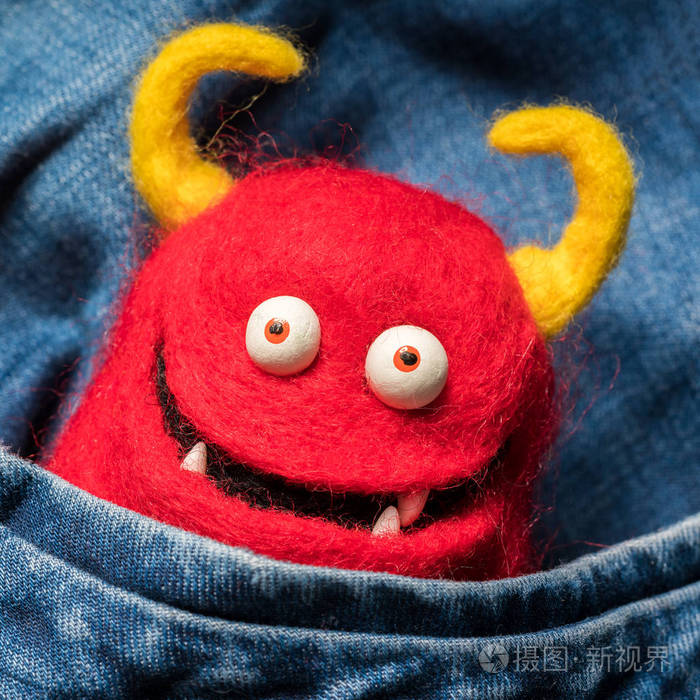 滑稽的红色魔鬼玩具在口袋里的牛仔裤