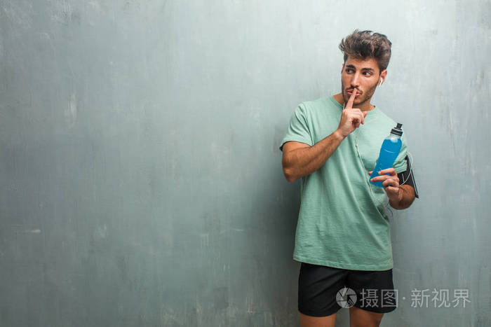 年轻的健身男子对一个垃圾墙保持一个秘密或要求沉默, 持有蓝色能量饮料