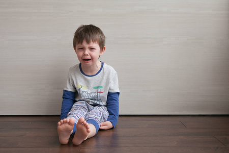 那男孩心烦意乱, 哭着, 抗议。坐在地板上的房间里