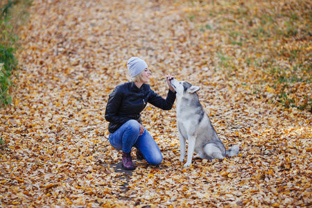 美丽的白种女孩在秋天森林或公园与沙哑的狗玩