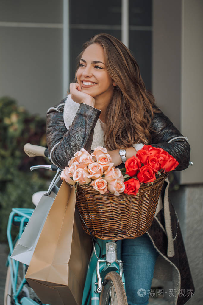 美丽的年轻微笑的妇女与她的自行车和购物袋在城市。美容时尚和生活方式