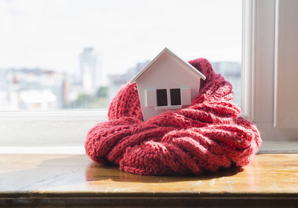 住宅在冬天供暖系统概念和冷的下雪的天气以房子的模型佩带毛线帽