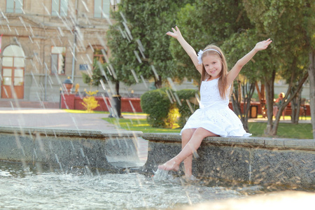 快乐与美丽的头发的年轻女孩才子英尺的喷泉在炎热的夏天一天
