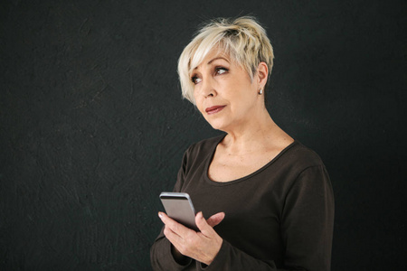 一位积极的现代老年妇女手持手机, 正在使用它。老一辈与现代科技