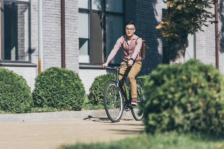 亚洲年轻人背包骑自行车在街上