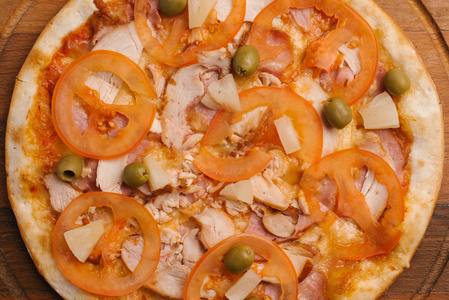 与番茄酱芝士鸡肉火腿西红柿菠萝片和橄榄一起在木制披萨盘上的小比萨