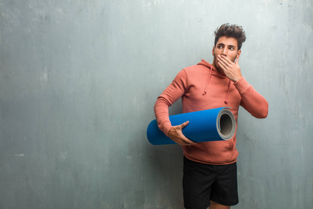 年轻健身男子对一个垃圾墙覆盖口, 举行了一个蓝色的垫子练习瑜伽
