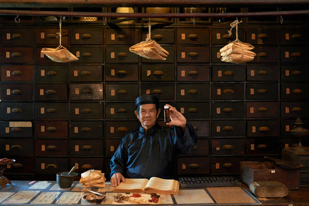 愉快的传统亚洲药剂师工作者显示瓶与医学照片