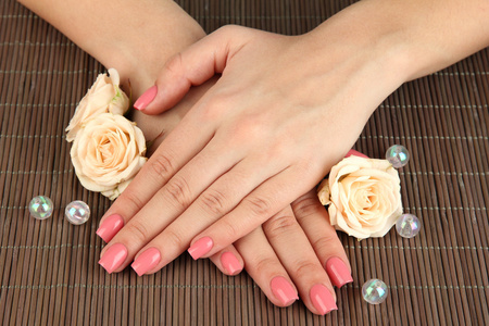 女人手中粉红色修指甲和鲜花的竹凉席背景