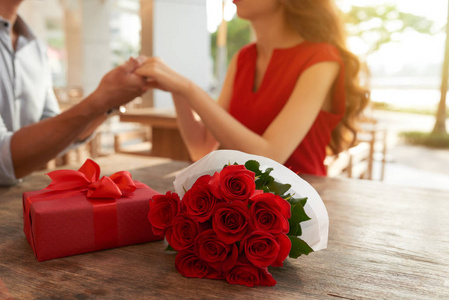情侣牵手的时候, 有浪漫的约会, 花束的红玫瑰和礼品盒躺在木桌上