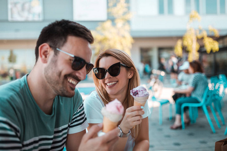 美丽的年轻夫妇与太阳镜是坐在户外和冰淇凌