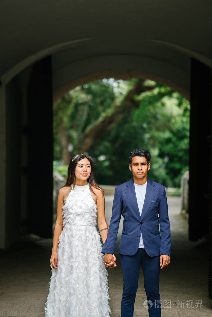 这对异族情侣在白天的拱门下拍照留念, 并微笑着