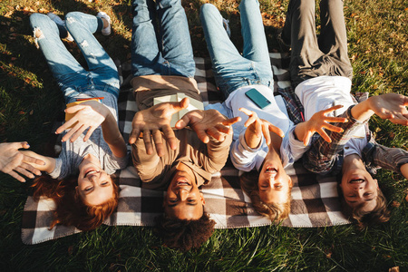一群快乐的 multhiethnic 学生躺在草地上, 拿着书, 张开双臂