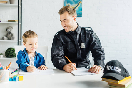 微笑的年轻父亲在警察制服和儿子在家里画画