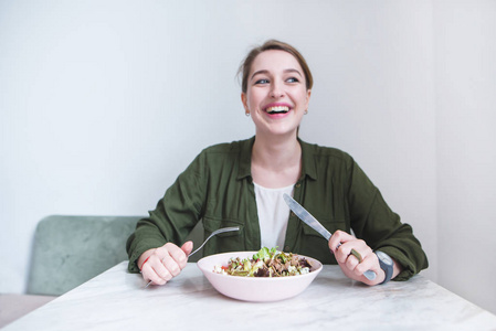 快乐的女人坐在桌子旁边的盘子里, 用有用的食物和微笑。专注于沙拉盘子
