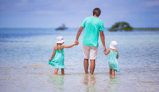 年轻的父亲的背影和他两个孩子在海边散步
