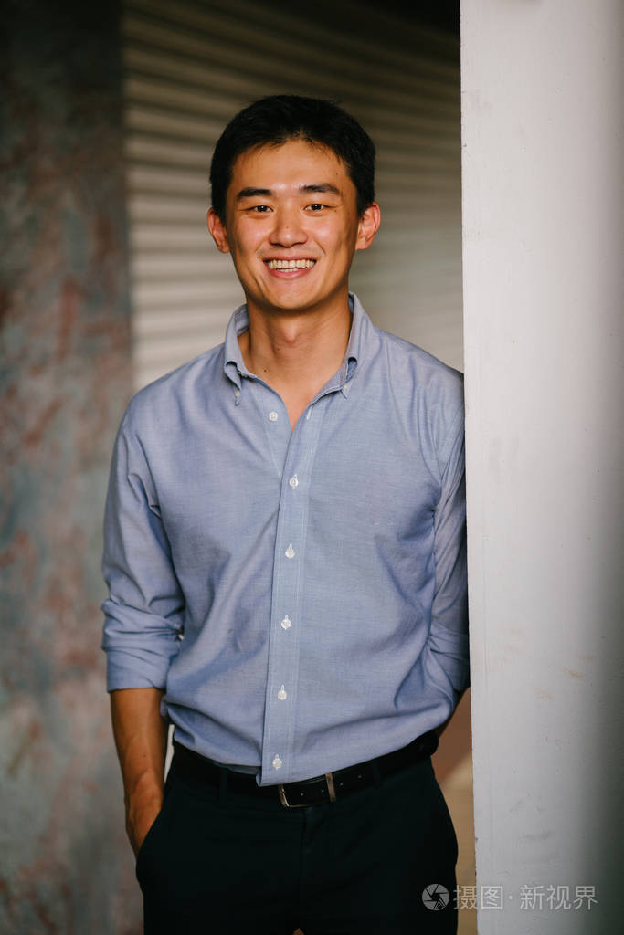 一个英俊, 年轻, 聪明的中国亚裔男子的肖像微笑着, 站在墙上的一天.